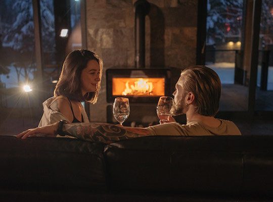 A couple sitting in front of a fireplace and drinking wine