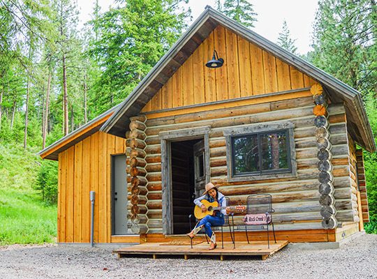 A Woman playing guitar in front of a log cabin
