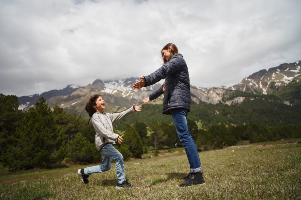 A woman and child playing in a green grass field near a mountain