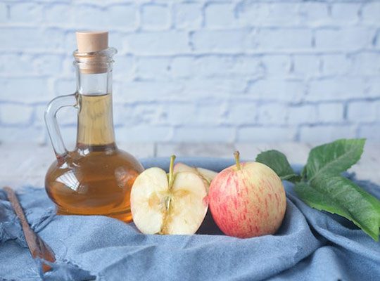 A glass jar containing juice next to sliced apples