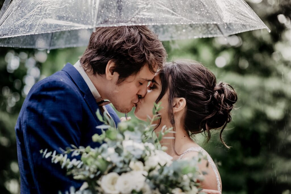A bride and groom kissing under an umbrella