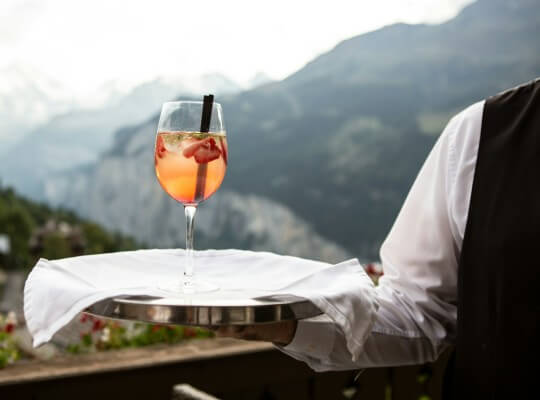 A waiter serving a cocktail with mountains in the background